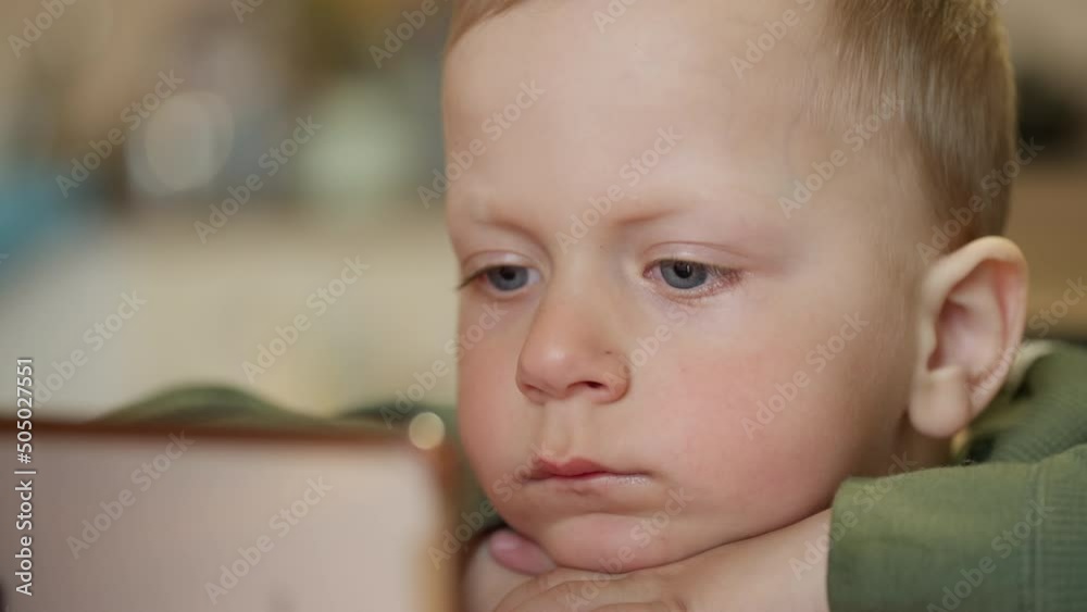 The child watches cartoons on the phone. Caucasian boy watching video on gadget. High quality 4k footage
