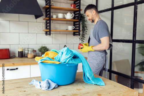 Handsome young strong man is washing dishes in the kitchen, doing laundry in his house. Male doing chore at home. Concept of sharing family housework between men and women, father and mother.