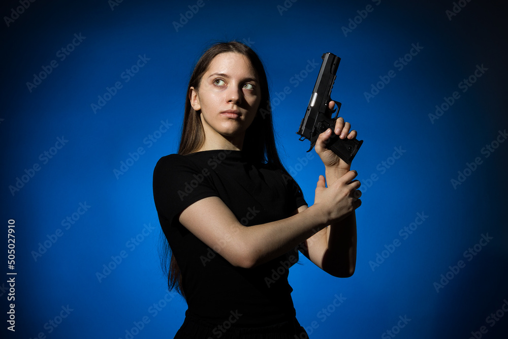 young beautiful woman with long hair in a black t-shirt with a gun on a blue background