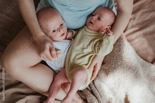 mother holding two twin babies in bed at home