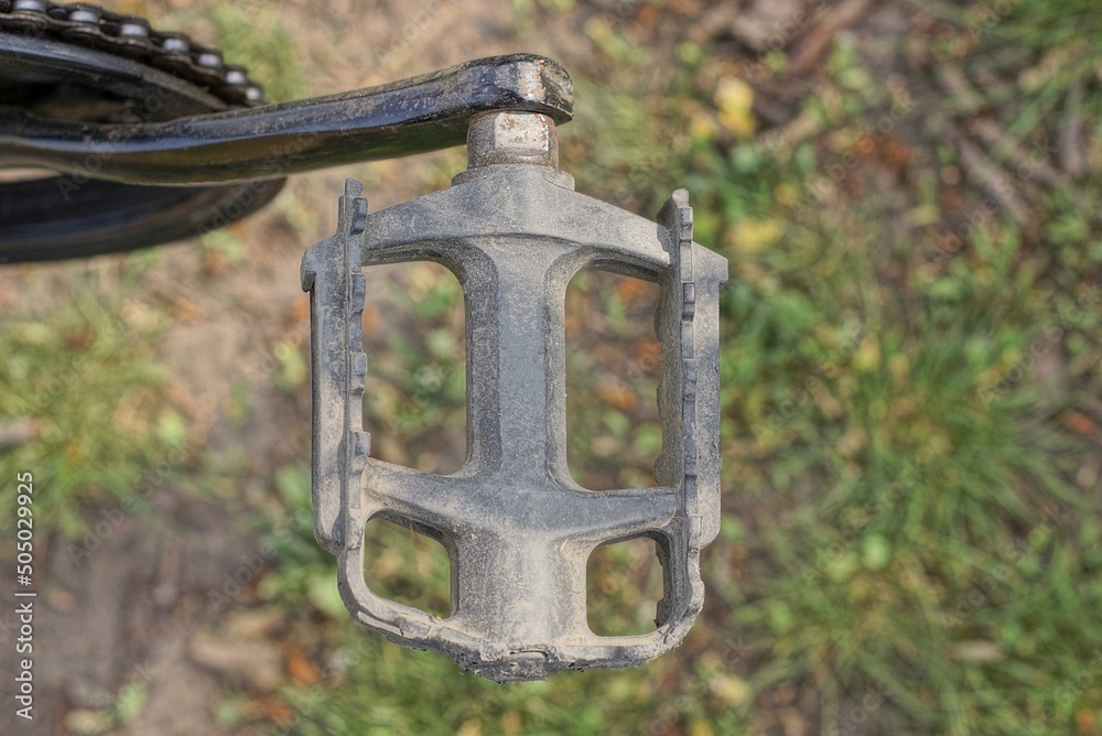 Fototapeta premium one gray metal pedal on a bicycle on the background of green grass on the street