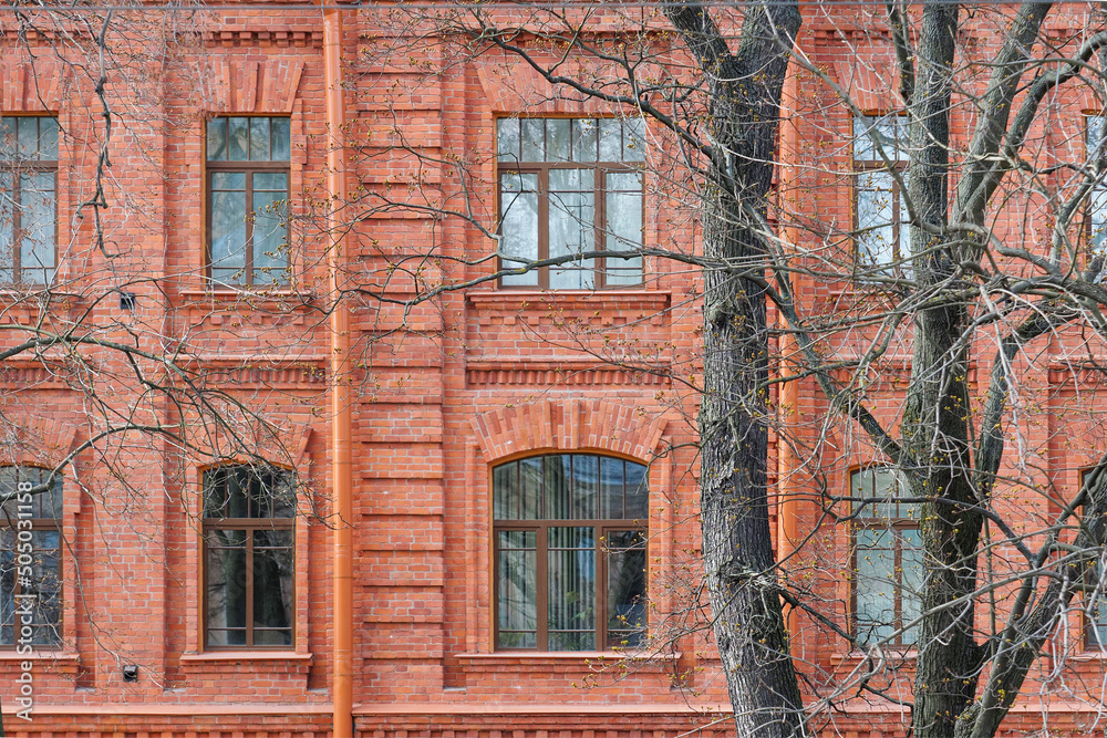 Old classic red brick building, trees growing in front of the building in early spring