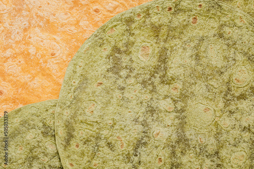 Tomato, spinach flavored wheat tortilla wraps. Spanish or Mexican circular unleavened flatbread from wheat flour. Ingredient for cooking fast food or snack. Closeup, texture background photo