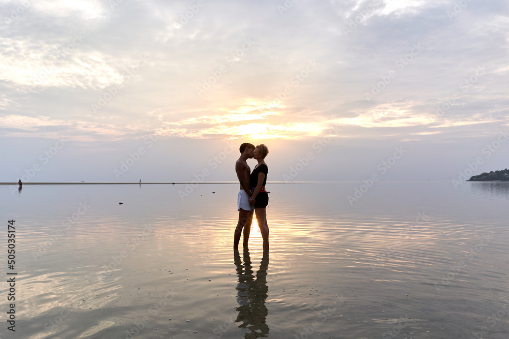 Silhouette of a couple kissing into the sea at sunset.