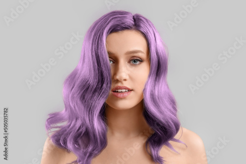 Beautiful young woman with purple hair on grey background photo