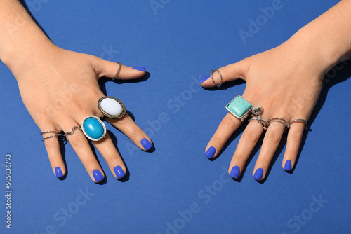 Hands with beautiful manicure and stylish jewelry on blue background