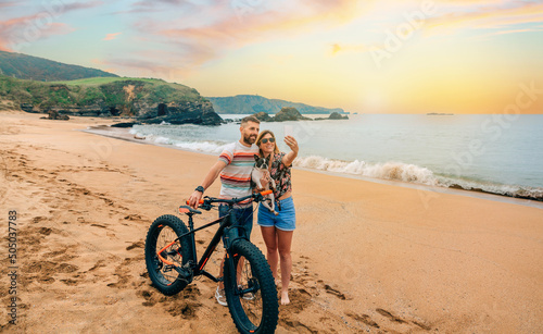 Young couple with fat bike taking a selfie with their dog on the beach