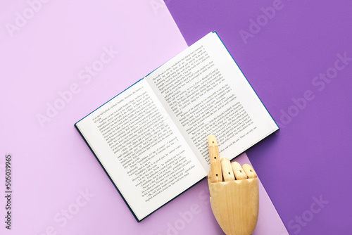 Wooden hand and open book on color background