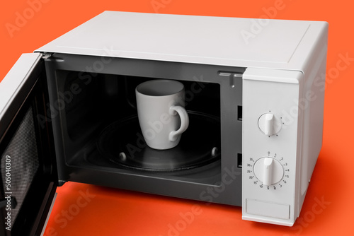 Cup in opened microwave oven on color background