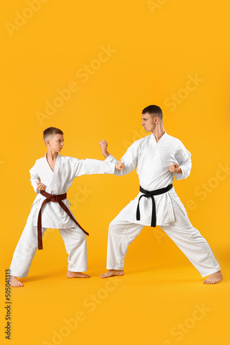 Boy practicing karate with instructor on yellow background photo