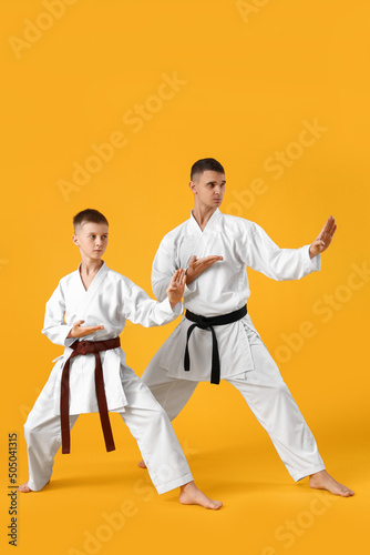 Boy practicing karate with instructor on yellow background