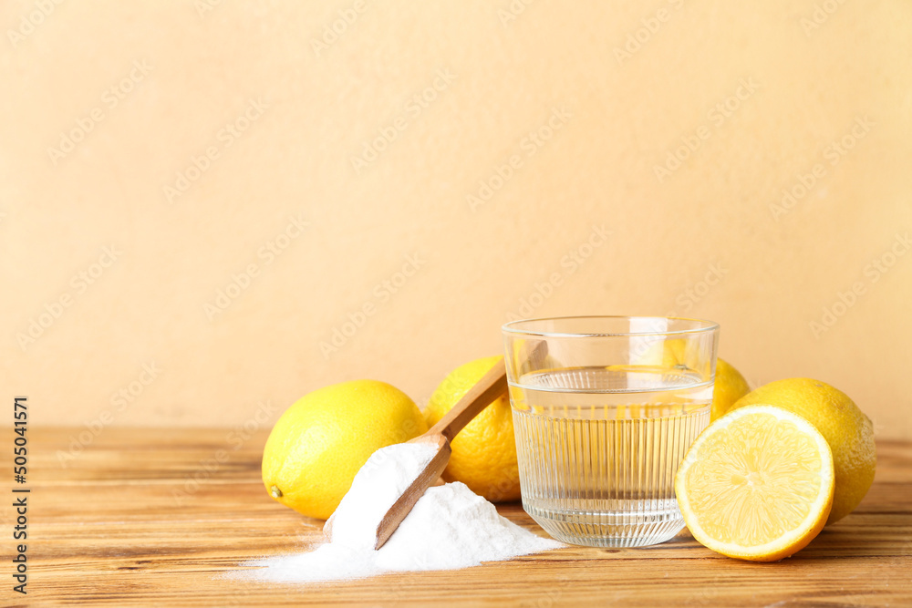 Heap of baking soda, glass with water and ripe lemons on wooden table
