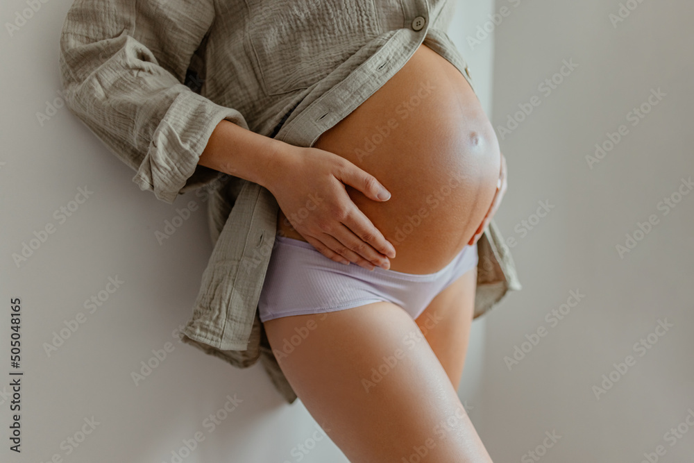 Pregnant woman wearing maternity underwear pajamas at home relaxing holding  expecting tummy for skincare, health, lifestyle. Pregnancy belly closeup  for cellulite and stretch marks Photos