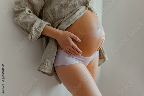 Pregnant woman wearing maternity underwear pajamas at home relaxing holding expecting tummy for skincare, health, lifestyle. Pregnancy belly closeup for cellulite and stretch marks photo