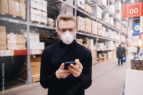 Young manager of store, man supervisor with protective mask using phone working in postal center warehouse