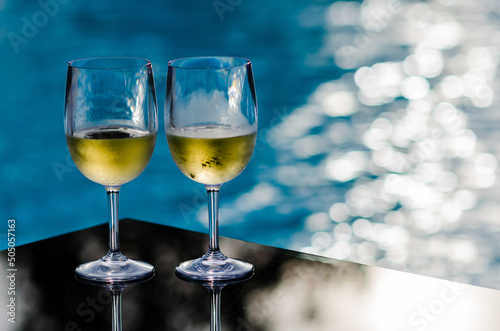 Two glasses of white wine put on table at swimming pool for Holiday and summer drink concept.