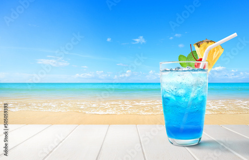 Blue hawaii cocktail on white wooden table with blue sea and sky background.