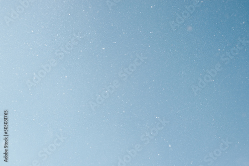 Falling snow, white snowflakes on clear blue sky outdoors. Defocus light slow snowfall in winter