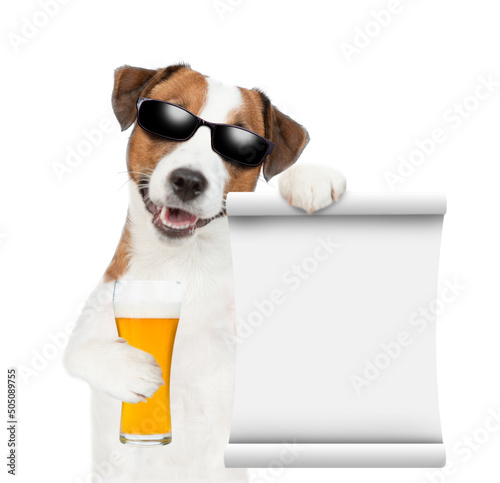 Jack russell terrier puppy wearing sunglasses holds mug of beer and empty list. isolated on white background