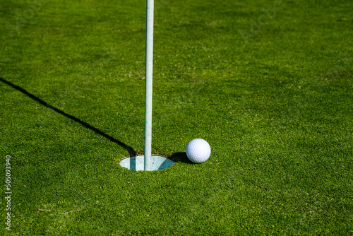 Golf ball on lip of cup on grass background. Golf hole. Golf ball on the lawn. Sport golf background with copy space.