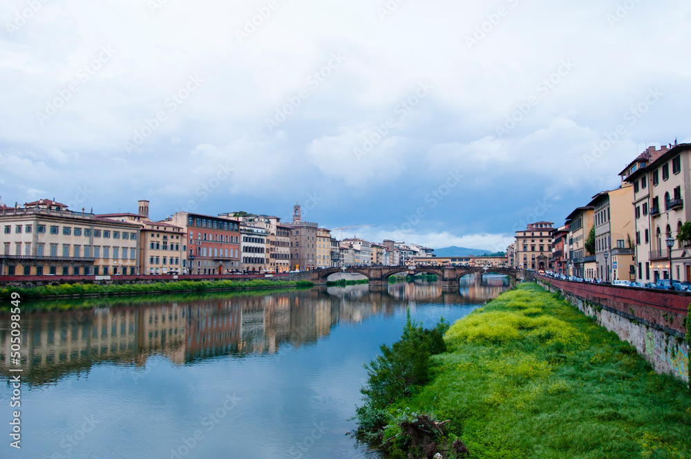 Fototapeta premium Overgrown Arno river bank with Ponte Santa Trinita StTrinity bridge and Florence cityscape in Italy