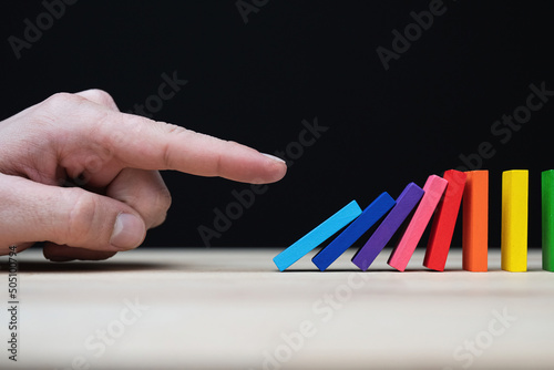 Conceptual photo of a hand starting a chain reaction with colored dominoes.
Domino effect with colored stones and copyspace. 