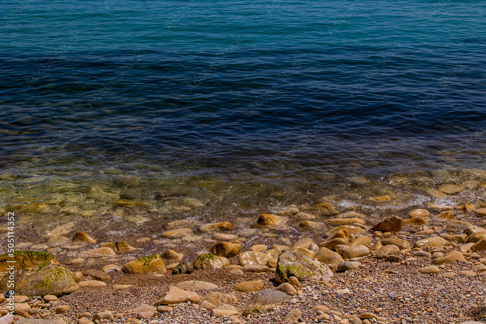 calm gentle background of blue sea and shore with beige stones calm gentle background of blue sea and shore with beige stones