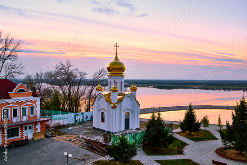 Orthodox church on the territory of the Zaimka tourist complex against the background of a bright sunset over the Ussuri River near the city of Khabarovsk. Russia. photo