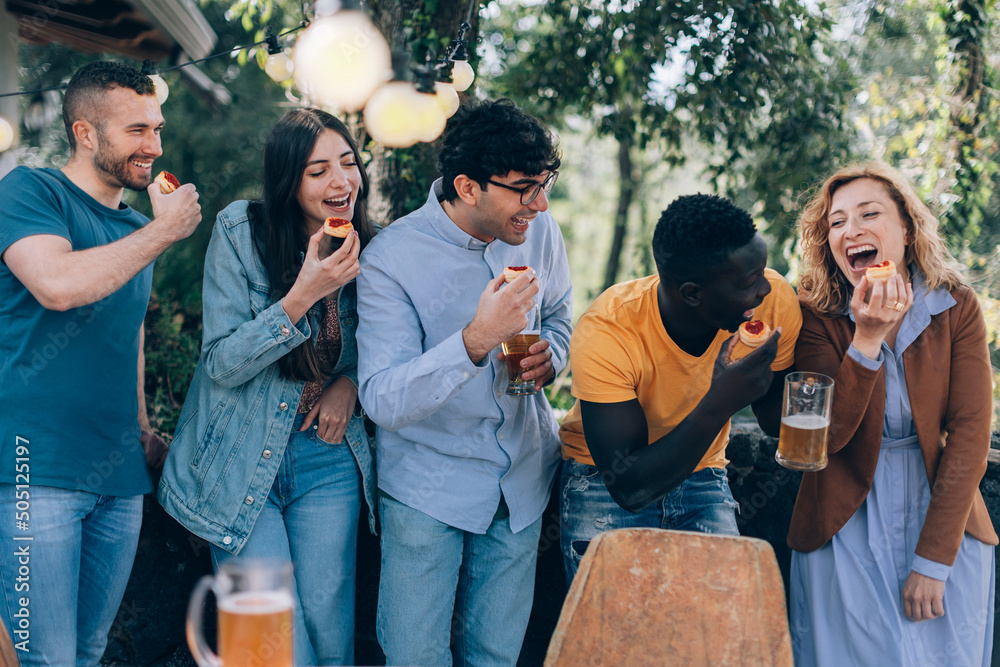 Obraz premium people having fun - happy friends playing with food - glamping party with small pizzas and beer - holiday concept