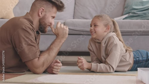 Slowmo of modern father arm wrestling with his little daughter and letting her to win, lying on rug in living room photo