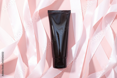 Black squeeze bottle cosmetic tube and pink ribbons on pink background, mockup. Daily cream, gel, skin care, sunscreen, moisturizer. Front view, blank bottle.