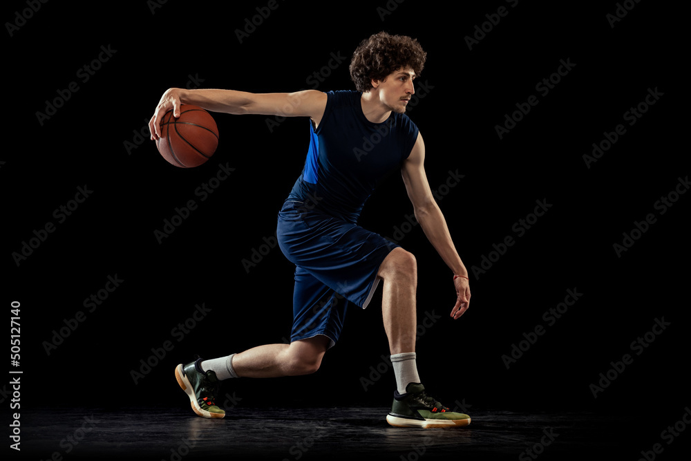Professional basketball player in action and motion isolated on dark background. Concept of sport, competition, achievements, game.