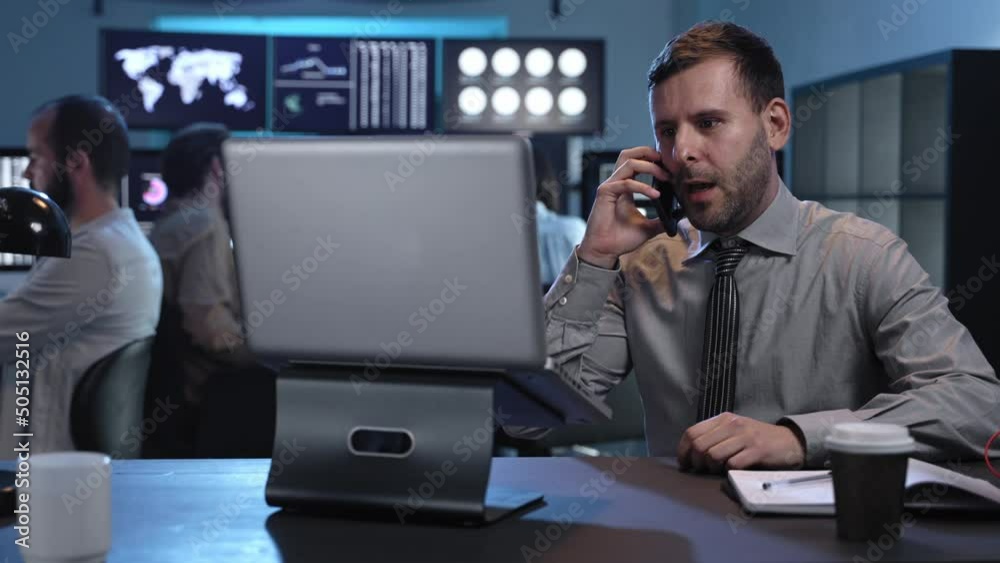 Successful trader businessman on a phone call investing in stock market using computer screens in busy modern office. Hesitate before decision in investment Successful trader businessman on a phone call investing in stock market using computer screens in busy modern office. Hesitate before decision in investment