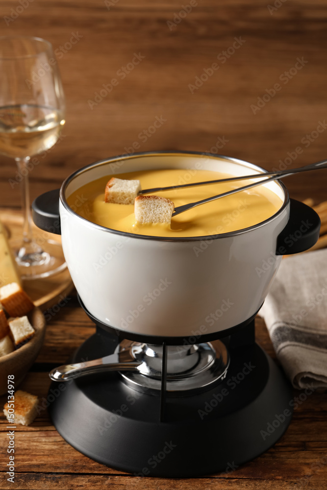 Pot of tasty cheese fondue and forks with bread pieces on wooden table - obrazy, fototapety, plakaty 