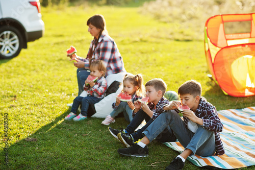 Family spending time together. Four kids with mother eat watermelon outdoor.