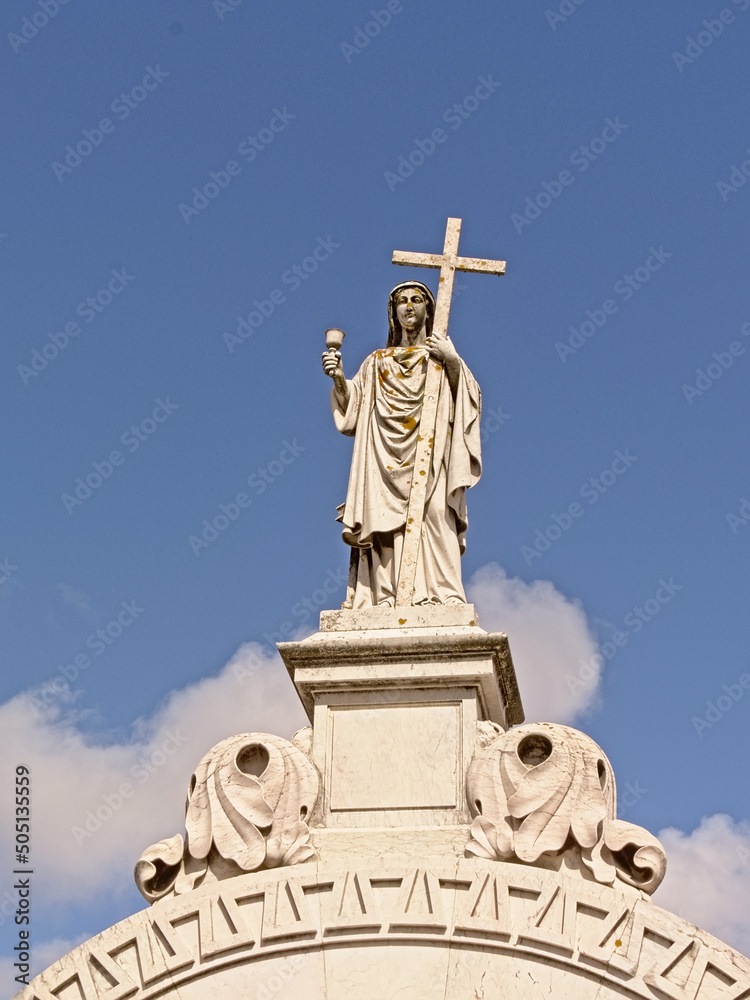 Statue of Jesus christ holding a cross on top of a grave tomb in Altode Sao Joao cemetery, Lisbon
