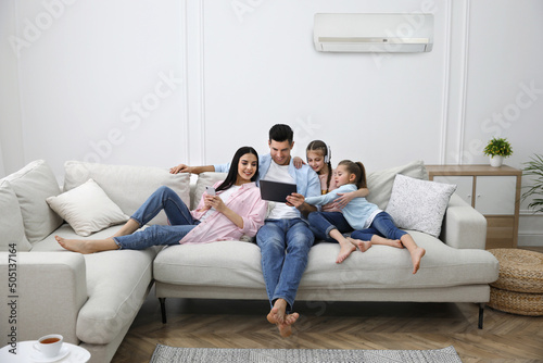 Happy family resting under air conditioner on white wall at home photo