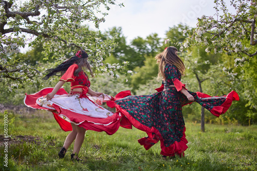 two dancers in traditional gypsy dresses dance in nature on a spring day