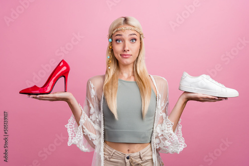Portrait of attractive skeptic minded girl holding on palms choosing shoes isolated over pink pastel color background