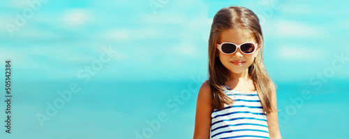 Summer portrait of smiling little girl child wearing striped dress on beach on sea background, blank copy space for advertising text