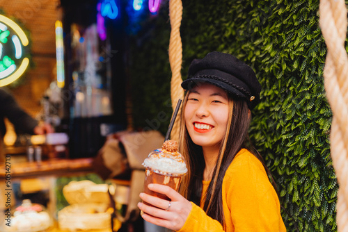 portrait of young chinese girl looking at camera smiling and drinking special coffee with chocolate and cream in modern coffee shop.