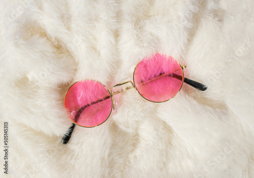 Creative retro idea made of neon pink lennon sunglasses on white fur. Summer party or 90s fashion concept.