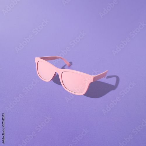 PInk sunglasses with sunlight shadow on purple background. Minimal summer vacation convcept.