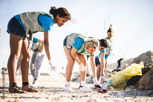 Diverse people cleaning up the beach, volunteers collecting the waste on the coast line, young people working in team aware of the pollution produced by the plastic industry