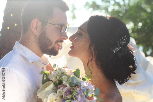 An incredibly beautiful brunette and a bearded guy in glasses kiss at sunset on their wedding day. Two lovers on a romantic date. Love background concept