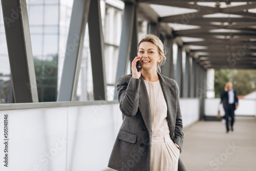 Portrait of a beautiful mature business woman in suit and gray jacket smiling and talking on the phone on a modern urban and office buildings background