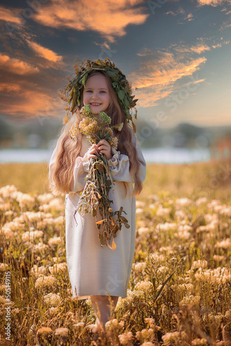 Portrait of a cute village girl kid щт sunsetin a wreath on a flower field. A child in a blooming meadow. photo