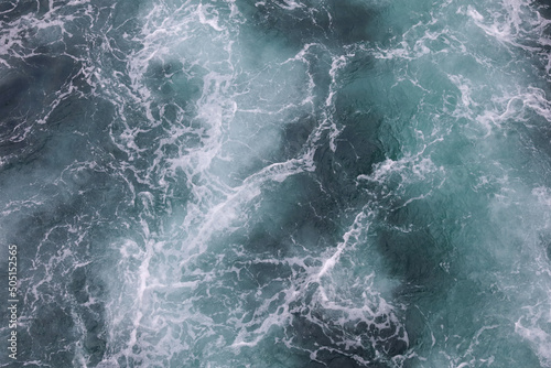 Water surface abstract background. White waves and foam on the blue sea water. Wake behind ship
