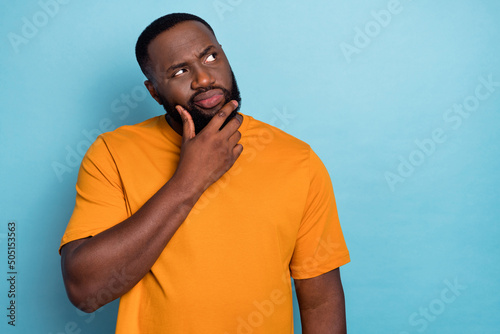 Photo of doubtful unsure guy dressed orange t-shirt looking empty space arm chin isolated blue color background photo