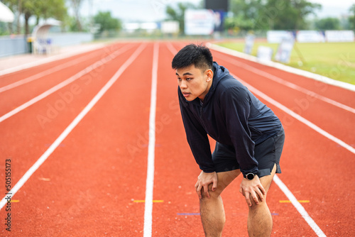 Young chinese man tired during jogging on the track in sport stadium. Young asian male intense training workout challenge breathing exhausted. Healthy and active lifestyle concept.